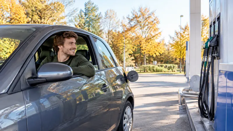 Junger Mann hält mit seinem Kleinwagen an einer Zapfsäule, die Tankklappe zeigt zur richtigen Seite